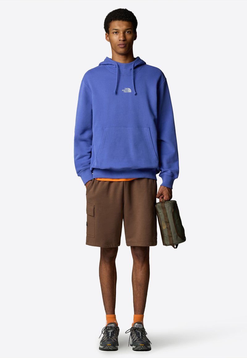 Kungsblå hoodie med känguruficka, kombinerad med bruna shorts med cargofickor. Orange strumpor och grå sportskor.