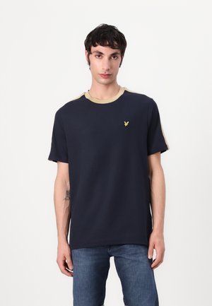 T-shirt en coton bleu marine avec un col rond et des accents beiges sur les épaules. Il présente un petit logo jaune sur la poitrine. Coupe décontractée.