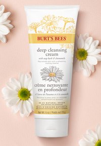 Burt's Bees diepe reinigingscrème in een witte tube met gele en grijze accenten, heeft bloemversieringen en toont de belangrijkste ingrediënten. 170 g.