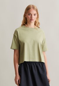 Olijfgroene cropped t-shirt met korte mouwen, textuurstof, ronde halslijn, gecombineerd met een donker rokje met elastische taille.