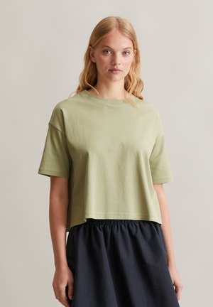 Olive green cropped t-shirt with short sleeves, textured fabric, round neckline, paired with a dark elastic-waist skirt.