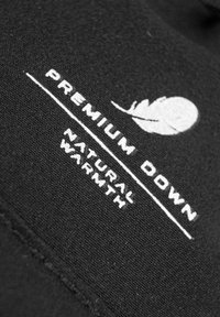 Tela negra con texto blanco que dice "PREMIUM DOWN" y "NATURAL WARMTH", acompañado de un gráfico de pluma simple. Superficie texturizada.
