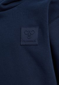 Marineblauwe stof met een zwarte patch met het geëmbossede hummel merklogo met een gestileerd bijensymbool.