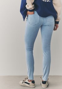 Svetlomodre ozke jeans hlače s klasičnim dizajnom s petimi žepi. Oblečene z mornarsko modrim in bež puloverjem ter nevtralnimi supergami. Gladek denim tekstura.