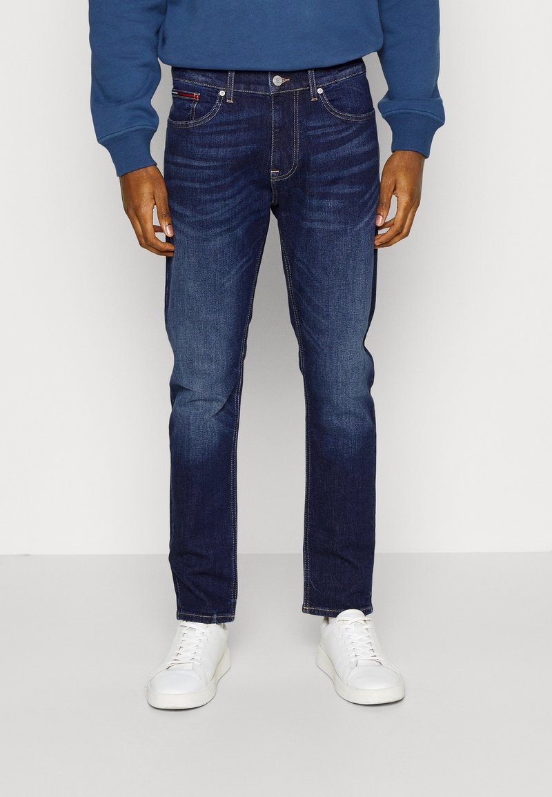 Mörkblå denimjeans med en klassisk passform, med framfickor, subtil blekning och ett midjeband med silverknappar. Matchad med vita sneakers.