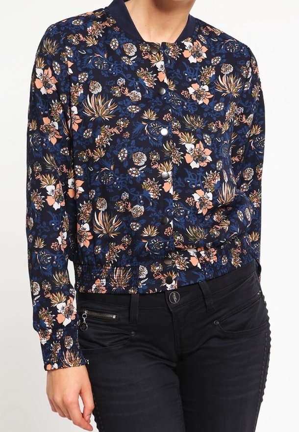 Marinblå blommig bomberjacka med en lätt åtsittande midja, prydd med rosa och gula blommönster samt svarta knappar, matchad med svarta jeans.
