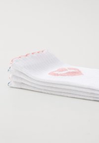Weiße Socken aus geripptem Stoff, mit einem rosa Lippenabdruck an der Seite und gewellten roten Akzenten oben.