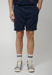 Pantalones cortos de algodón azul marino con dobladillos enrollados, que cuentan con un cierre de botón y bolsillos laterales, combinados con zapatillas altas de patrón y calcetines de rayas.