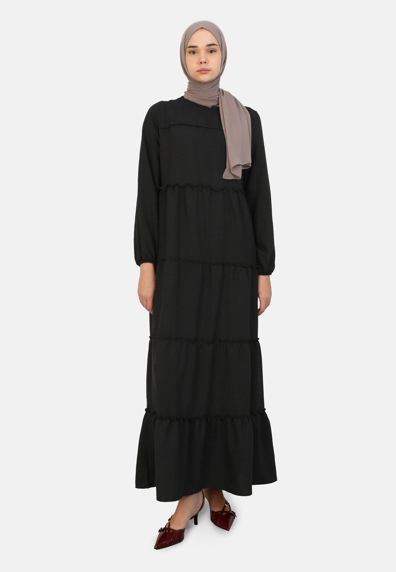 Gaun maxi hitam terbuat dari kain lembut, dengan lengan panjang, lapisan berenda, dan hem yang melebar. Dilengkapi dengan hijab abu-abu muda.