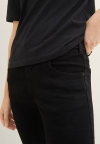 Jeans de mezclilla negra con un diseño ajustado, que presentan bolsillos frontales y costuras sutiles. Combinados con una camiseta negra holgada, confeccionada en un tejido suave.