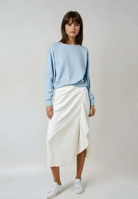 Sweatshirt surdimensionné bleu clair avec des poignets côtelés, associé à une jupe enveloppante blanche asymétrique ornée de rayures verticales et d'une texture douce.