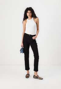 Črne jeans hlače s ravnim krojem, v kombinaciji z belo brezrokavnikom. Model drži modro torbico in nosi balerinke s leopardjim vzorcem.