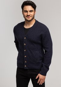 Ciemnoniebieski wełniany kardigan z dekoltem w serek, zapięciem na sześć guzików, prążkowanymi mankietami i naszywaną kieszenią po lewej stronie.