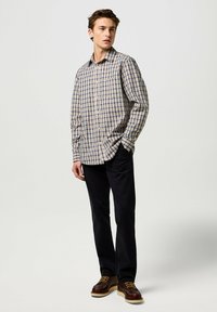 Heren overhemd met lange mouwen in een geruite stof van blauw, geel en wit. Gecombineerd met donkere broek en bruine schoenen.
