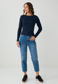 Marineblauw langslavige top met een geribbelde textuur, gecombineerd met lichtblauwe high-waisted jeans met een rechte pijp en een rafelige zoom. Zwarte sportschoenen.