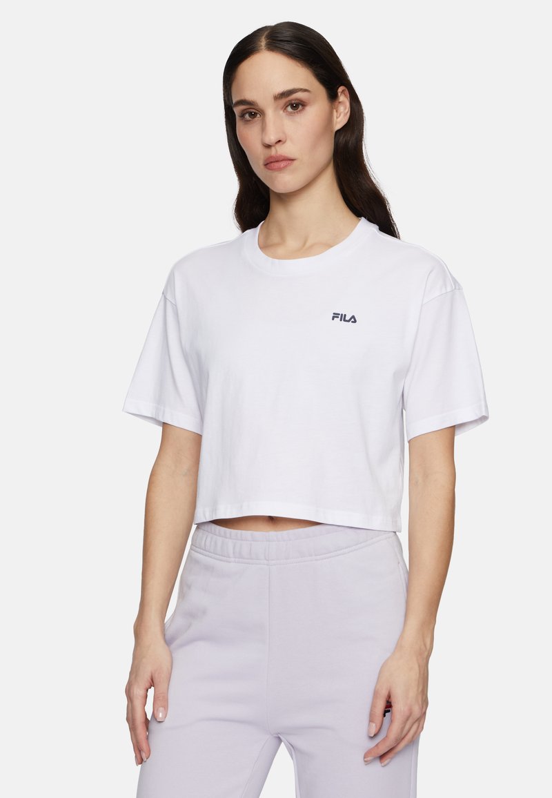 T-shirt cropped in cotone bianco con maniche corte, caratterizzato da un piccolo logo FILA navy sul petto sinistro. Tessuto morbido, vestibilità comoda.