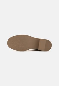 Semelle en caoutchouc marron avec un motif de grip texturé, talon légèrement surélevé et finition lisse. La surface est propre sans marquages visibles.