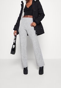 Svart parka med pälsfoder, grå bootcut-byxor i mjukt strukturerat tyg och svarta platåstövlar. Håller en liten glänsande svart väska.