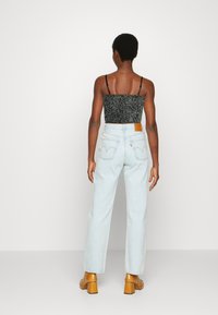 Top preto texturizado cortado, jeans de cintura alta azul claro com bolsos traseiros, etiqueta de couro castanho e sapatos de salto bloco bege.