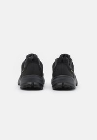 Czarne buty sportowe z teksturowanym wykończeniem, wyściełanym kołnierzem i wzmocnioną piętą, z solidną podeszwą i minimalnymi akcentami.