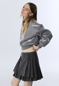 Gray sequined sweatshirt with a cropped design, paired with a pleated dark gray skirt featuring drawstring details at the waist.