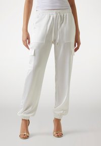 Vita satin joggingbyxor med elastiska muddar, två framfickor och dragsko i midjan. Slät textur och avslappnad passform. Guldiga detaljer.