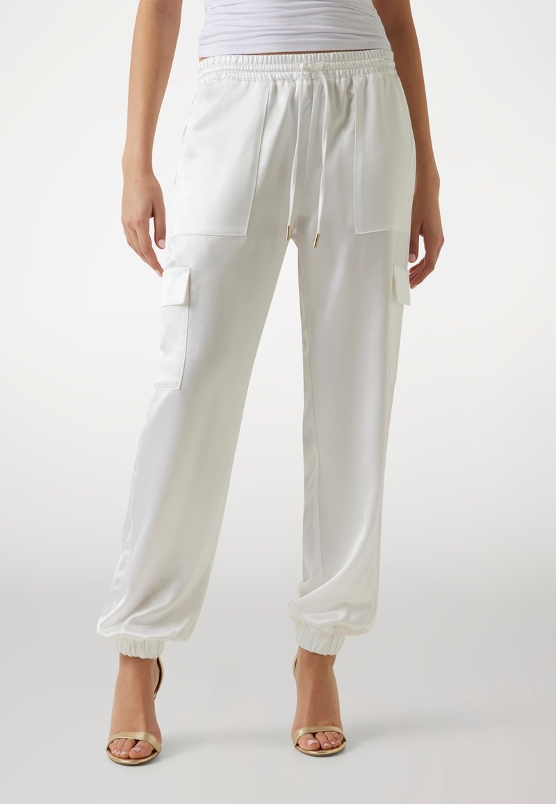 Vita satin joggingbyxor med elastiska muddar, två framfickor och dragsko i midjan. Slät textur och avslappnad passform. Guldiga detaljer.