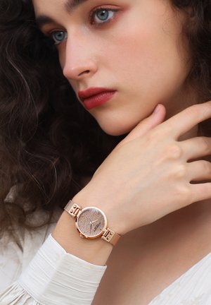 Rose gold wristwatch with a textured round face, metal mesh band, and minimalistic silver and rose accents, worn on a wrist.