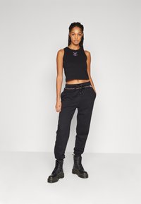 Top corto nero con ricami viola, abbinato a pantaloni jogger neri con vita regolabile e polsini elastici, indossato con stivali neri.