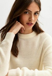 Maglione di colore crema con scollo a girocollo a coste e maniche lunghe, leggermente oversize. La texture è morbida e traspirante.
