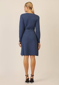 Abito blu lavorato a maglia con maniche lunghe, vita cintrata e gonna svasata. Tessuto testurizzato e delicate fessure laterali. Indossate sandali neri con tacco alto.