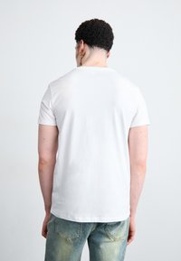 Simpel hvid t-shirt med korte ærmer lavet af bomuld. Bagview viser en klassisk pasform med rund halsudskæring og glat tekstur. Båret med slidte blå jeans.