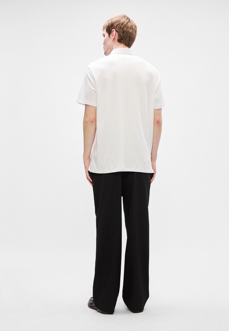 Chemise blanche à manches courtes pour homme au fit classique, associée à un pantalon large noir. Tissu lisse et design minimal sans motifs.