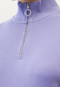 Haut col montant côtelé lilas avec fermeture à glissière partielle et anneau argenté. Le tissu présente une texture fine, soulignant une coupe ajustée.
