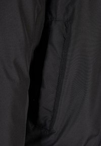 Chaqueta aislante negra con un exterior liso, un bolsillo oculto y un acabado mate, con detalles de costura a lo largo de las costuras.