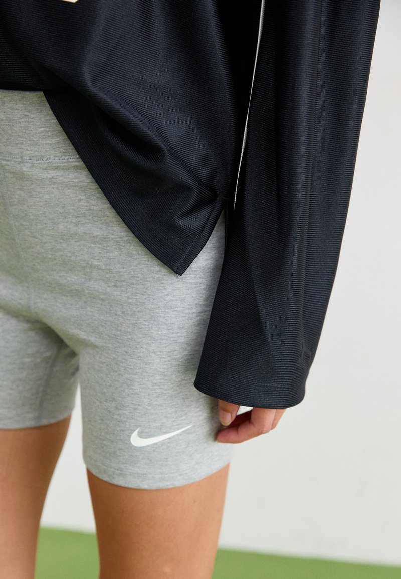 Haut noir à manches longues avec un tissu texturé, associé à un short gris avec un logo Nike blanc. La tenue met l'accent sur le confort et les vêtements de sport.