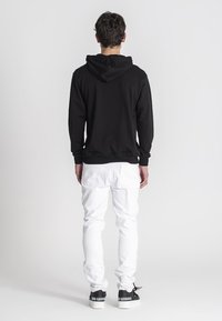 Čierna mikina s klokaním vreckom, rebrovanými manžetami a lemom, v kombinácii s bielymi džínsami a čiernymi teniskami so znakom na päte.