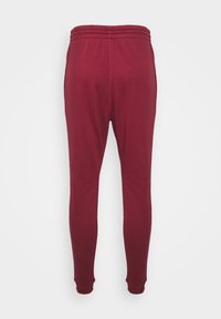 Burgundy joggers med en mjuk textur, elastisk midja med dubbel söm och figursydda muddar vid anklarna. Bakifrån visad.