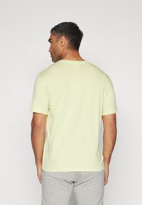 Helles gelbes T-Shirt mit kurzen Ärmeln und Rundhalsausschnitt, das eine glatte Textur und eine lockere Passform aufweist. Die Rückansicht zeigt ein simples Design.