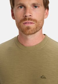 Olive green t-shirt with a round neck and short sleeves, made from a textured fabric, featuring a small logo on the chest.