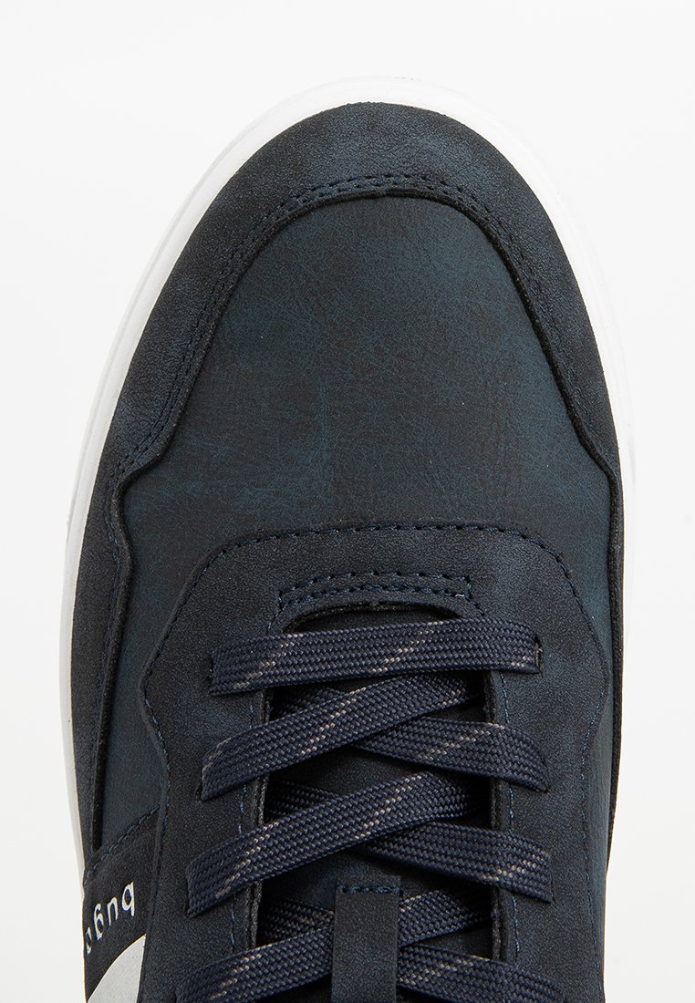 Zapatillas azul marino con parte superior de imitación de cuero, punta redondeada, cordones tejidos y suela de goma blanca. Presenta texturas sutiles y detalles de costura.