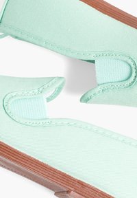 Groene canvas sandalen met een gestructureerd oppervlak en een bruine rubberen zool. Voorzien van twee verstelbare lussen voor het bevestigen van de voet.