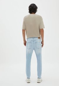 Camiseta de algodón color beige claro con mangas cortas, combinada con unos jeans de mezclilla azul claro con un lavado desgastado y bolsillos traseros. Zapatillas grises.