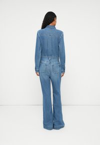 Denim jumpsuit in light blue, featuring a collared neck, long sleeves, a fitted waist, and flared trousers, with back pockets and seams.