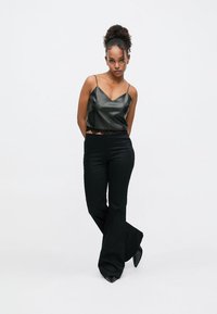 Top negru din piele cu bretele subțiri, asortat cu pantaloni evazați negri, cu talie înaltă. Textură netedă, siluetă ajustată și design elegant.