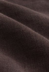 Gros plan d’un tissu tissé marron foncé plié montrant une surface texturée et des ombres douces.