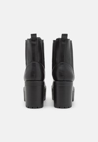 Botines de piel negra con punta redonda, paneles laterales elásticos y un tacón grueso texturizado. Presentan un acabado liso y lengüetas para tirar.