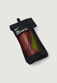 Funda negra para espinilleras Nike Mercurial Lite con una parte frontal transparente, que muestra una espinillera roja con un diseño texturizado y un acento verde.