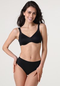 Reggiseno nero con coppe morbide e imbottite e spalline larghe; abbinato a slip neri a vita alta coordinati. Texture liscia, design senza cuciture.