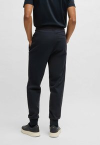 Mörkgrå träningsbyxor med resårmidja, smalnande ben och sidofickor, i kombination med svarta sneakers. Slät tyg utan synliga mönster.